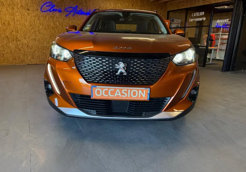 Vue de face d'un Peugeot 2008 orange métallisé avec calandre noire et phares LED allumés en showroom.