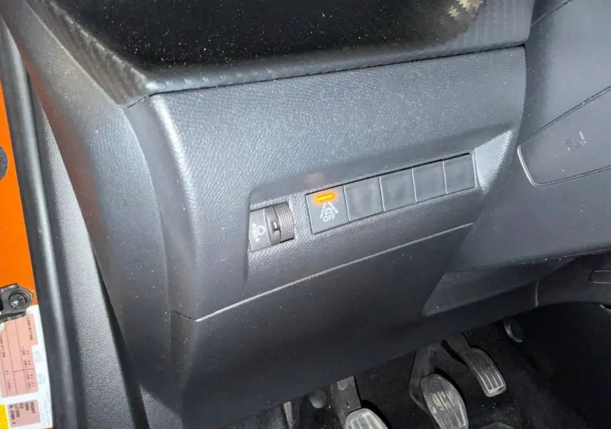 Détail du tableau de bord côté conducteur d’un Peugeot 2008 orange, avec commande d’assistance désactivée et pédales visibles.