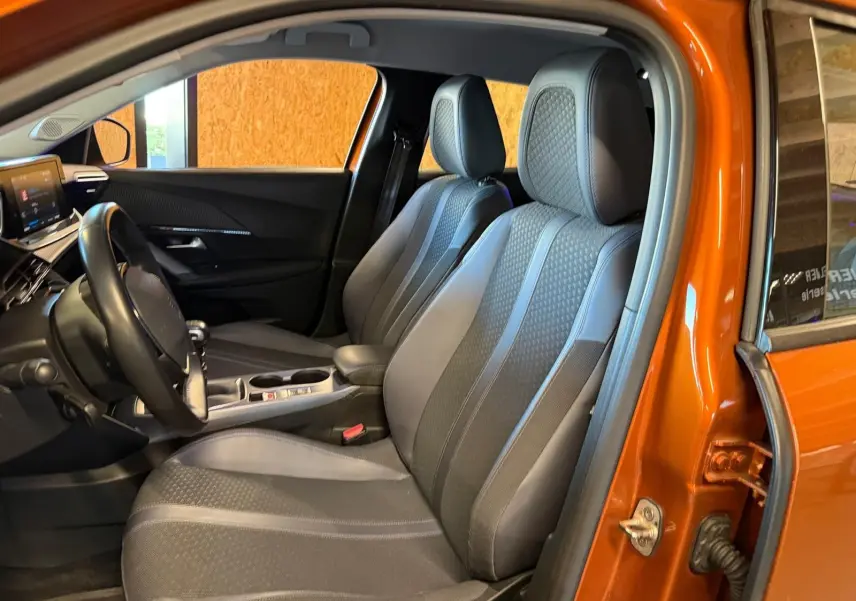 Vue intérieure côté conducteur de la Peugeot 2008 orange, montrant sièges tissu gris et volant compact cuir.