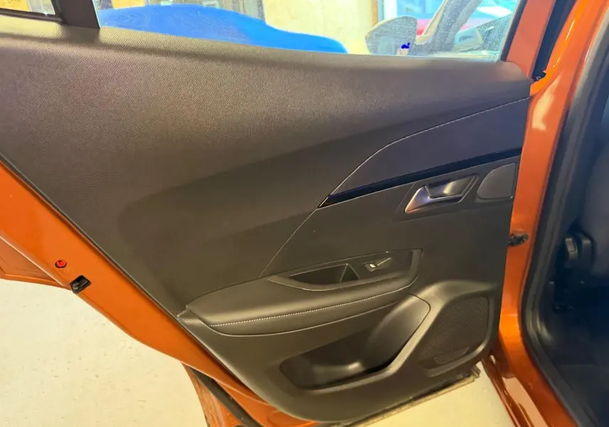 Vue intérieure de la porte arrière gauche orange du Peugeot 2008 1.5 BlueHDi 100 Allure avec garniture noire et commande de vitre.