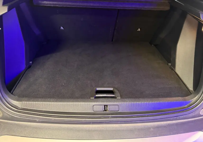 Coffre ouvert vu de l'arrière d'un Peugeot 2008 orange, espace de chargement vide et tapis noir.