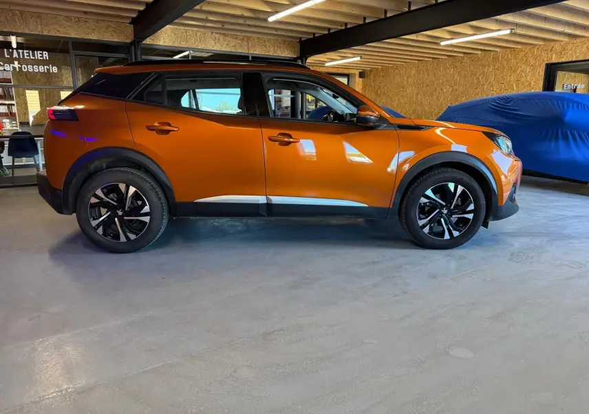 Peugeot 2008 orange vue de profil côté gauche, avec jantes alliage bi-ton et barres de toit noires.