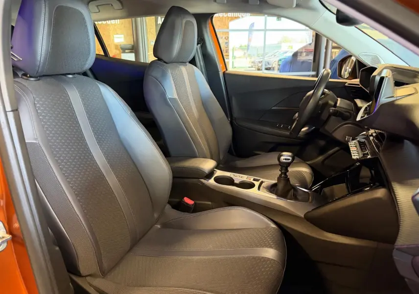 Vue intérieure côté gauche du Peugeot 2008 orange, montrant sièges tissu gris et levier de vitesse manuel.