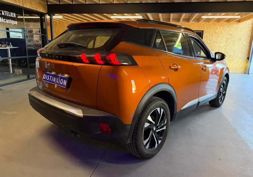Vue 3/4 arrière droite d’un Peugeot 2008 orange métallisé avec feux arrière LED en forme de griffes et jantes alliage bi-ton.