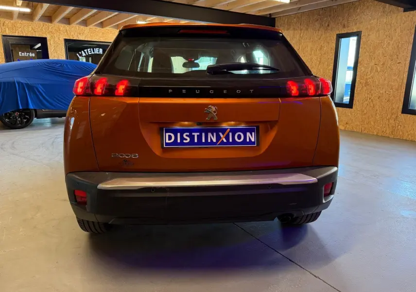 Vue arrière d'un Peugeot 2008 orange avec feux LED en forme de griffes et plaque Distinxion visible en intérieur.