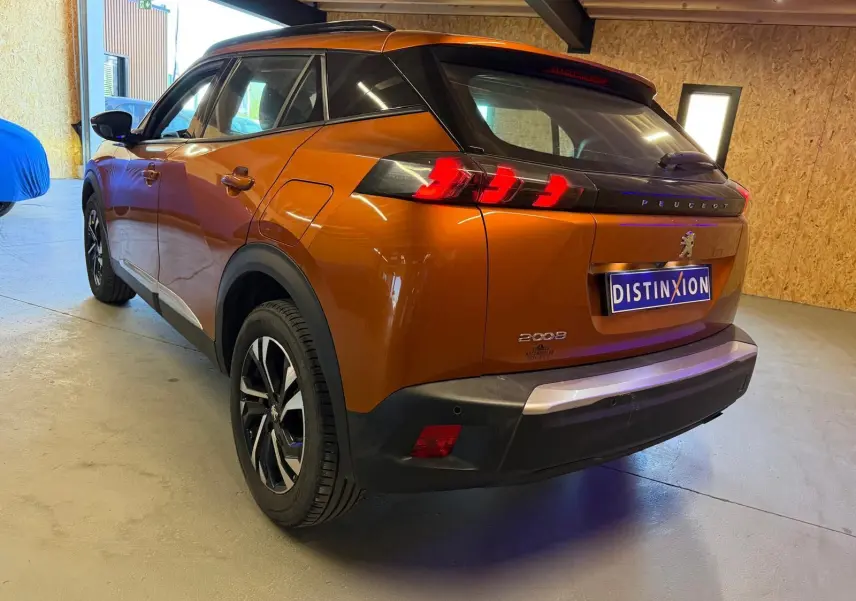 Vue 3/4 arrière droite d'un Peugeot 2008 orange métallisé avec feux arrière LED en forme de griffes et jantes alliage bi-ton.