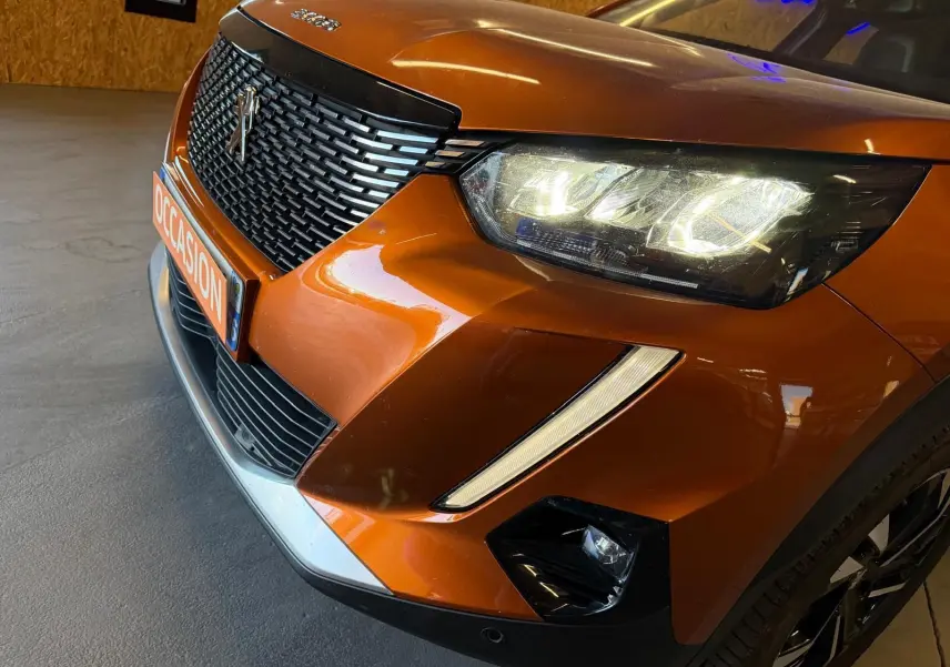 Vue 3/4 avant droit d’un Peugeot 2008 orange métallisé avec phares LED allumés et calandre noire distinctive.