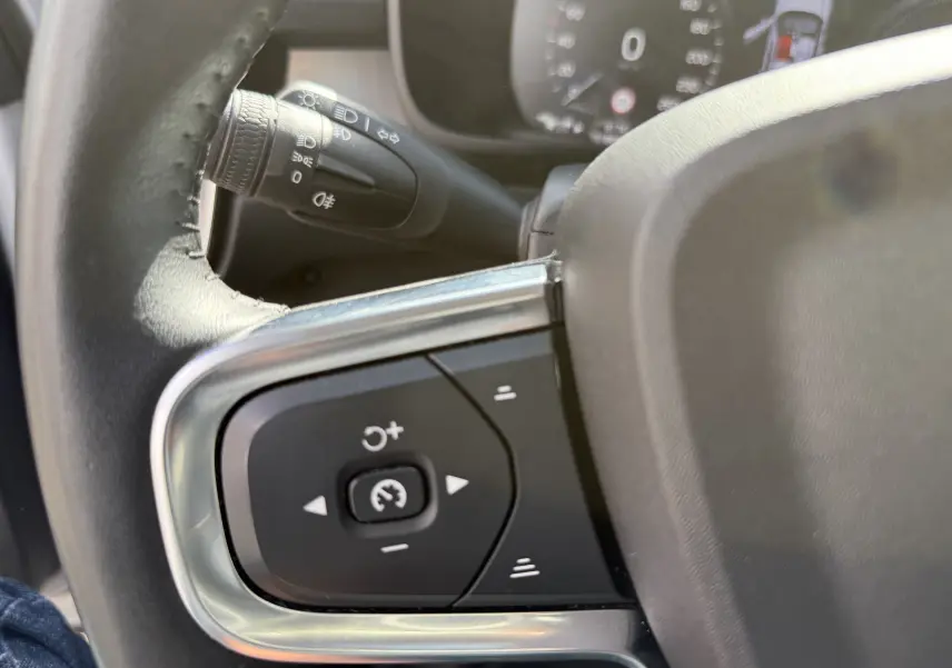 Gros plan sur les commandes de régulateur de vitesse au volant d’un Volvo XC40 blanc Crystal Metal, intérieur gris noir.