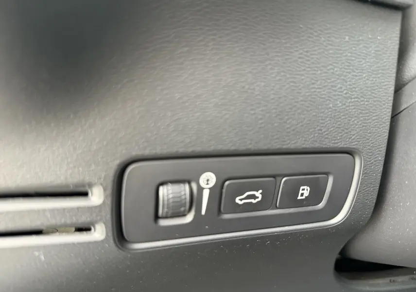 Gros plan sur les commandes d’ouverture du coffre et de la trappe à carburant dans un Volvo XC40 blanc Crystal Metal hybride rechargeable.