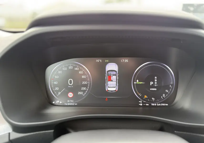 Tableau de bord numérique du Volvo XC40 blanc, affichant vitesse, mode hybride et état des portes à 17h35.