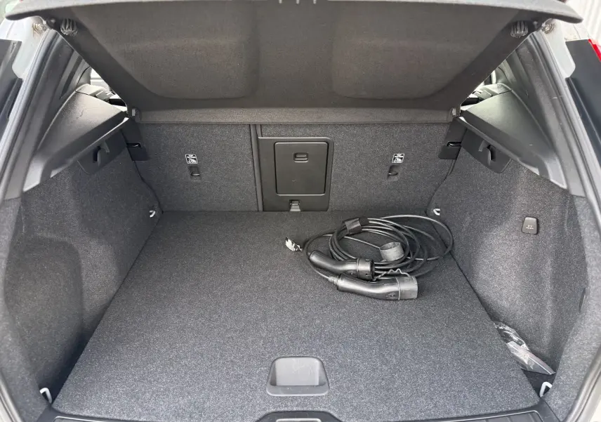 Coffre ouvert d’un Volvo XC40 hybride rechargeable blanc crystal metal, avec câble de recharge visible à droite.