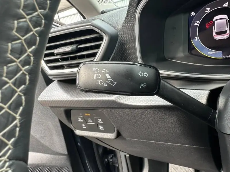 Gros plan sur la commande de clignotants à gauche du volant cuir noir dans l'habitacle gris/noir du SEAT Leon 2025.
