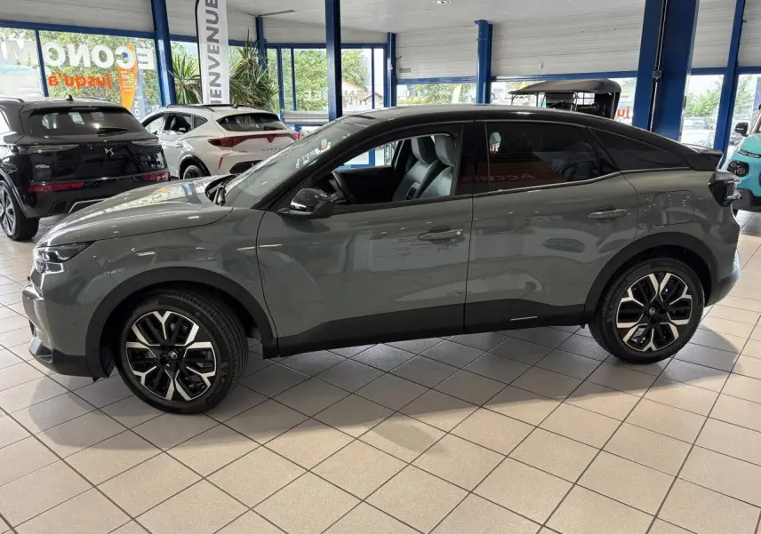 Profil côté gauche d'une Citroën C4 2026 vert Manhattan avec toit noir Perla Nera en showroom.
