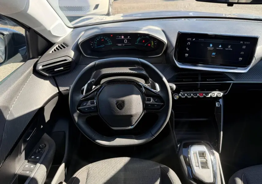 Vue intérieure frontale du poste de conduite de la Peugeot 208 gris Artense, avec volant compact et écran tactile central.