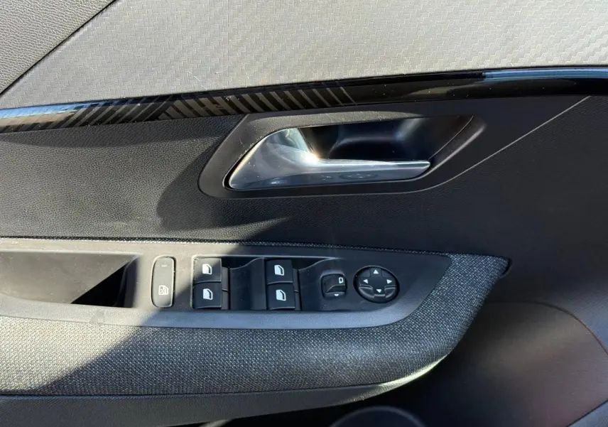 Gros plan sur la porte avant gauche de la Peugeot 208 1.2 Hybrid gris Artense, montrant les commandes des vitres et le bouton de réglage des rétroviseurs.