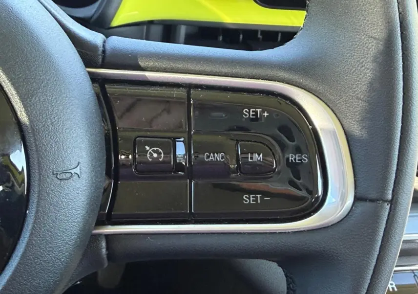 Gros plan sur les commandes de régulateur de vitesse au volant noir de la FIAT 500 e Ocean Green métal 2024.