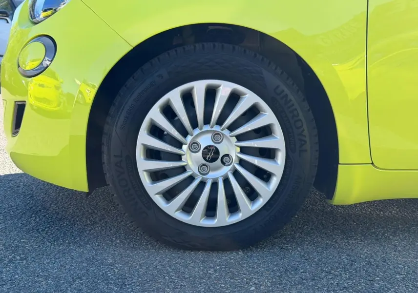 Gros plan sur la roue avant gauche d’une FIAT 500 électrique Ocean Green métal avec jante argentée à rayons fins.