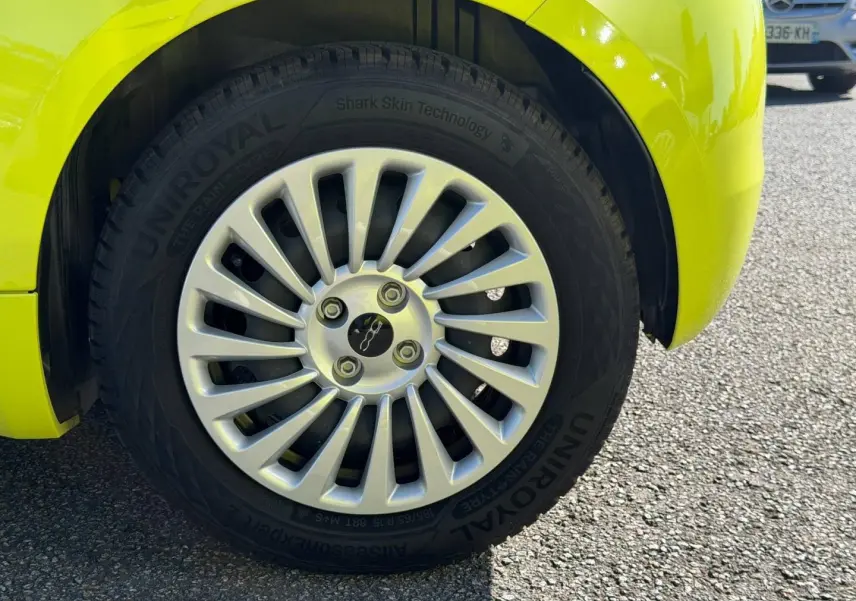Gros plan sur la roue avant droite d’une FIAT 500 électrique jaune vif avec jante argentée à rayons fins.