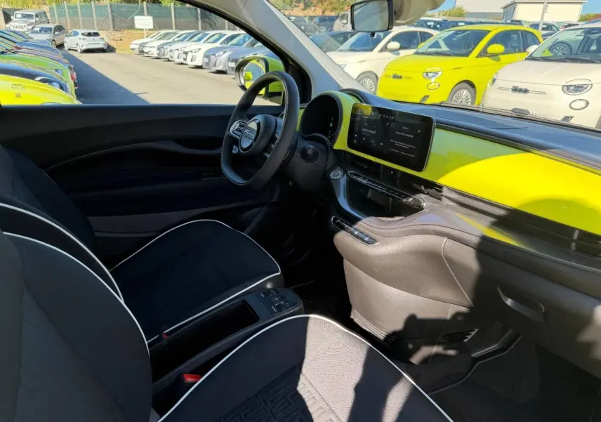 Vue intérieure côté conducteur de la Fiat 500 e 95ch Ocean Green avec tableau de bord jaune vif et sièges noirs.