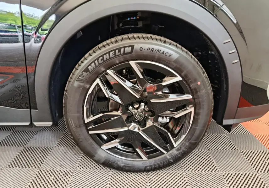 Gros plan sur la roue avant gauche noire du Peugeot 3008 1.2 HYBRID 145 GT avec jante en alliage chromée et pneu Michelin.