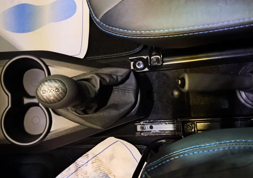 Gros plan sur la console centrale noire avec levier de vitesse et frein à main, sièges gris avec surpiqûres bleues visibles