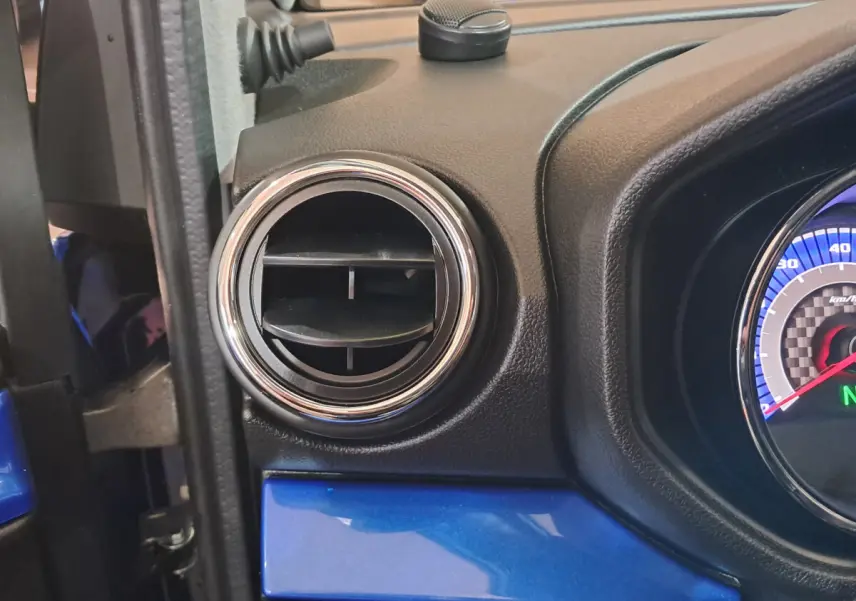 Détail de la sortie d'air ronde chromée côté conducteur sur tableau de bord bleu d'AIXAM AMBITION 2025.