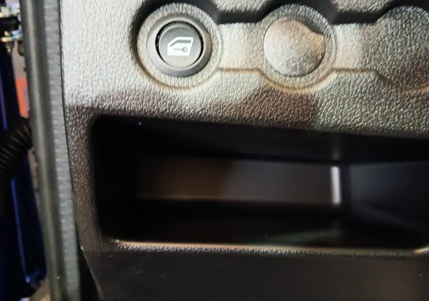 Gros plan sur le bouton d'ouverture du coffre dans l'habitacle d'une Aixam Ambition bleu 2025 côté conducteur.