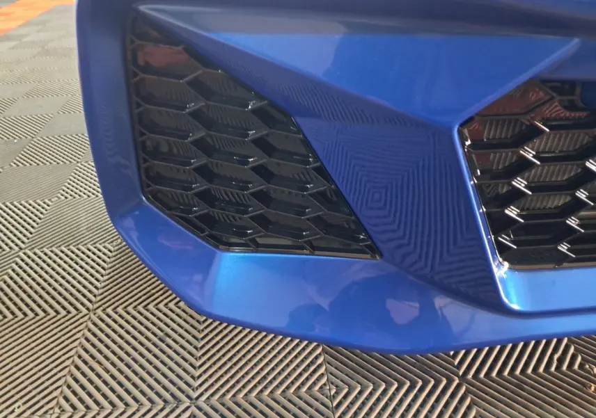 Gros plan sur la calandre avant gauche bleu métallisé de l'AIXAM AMBITION 0.5 CITY GTO 2025 avec grille noire hexagonale.