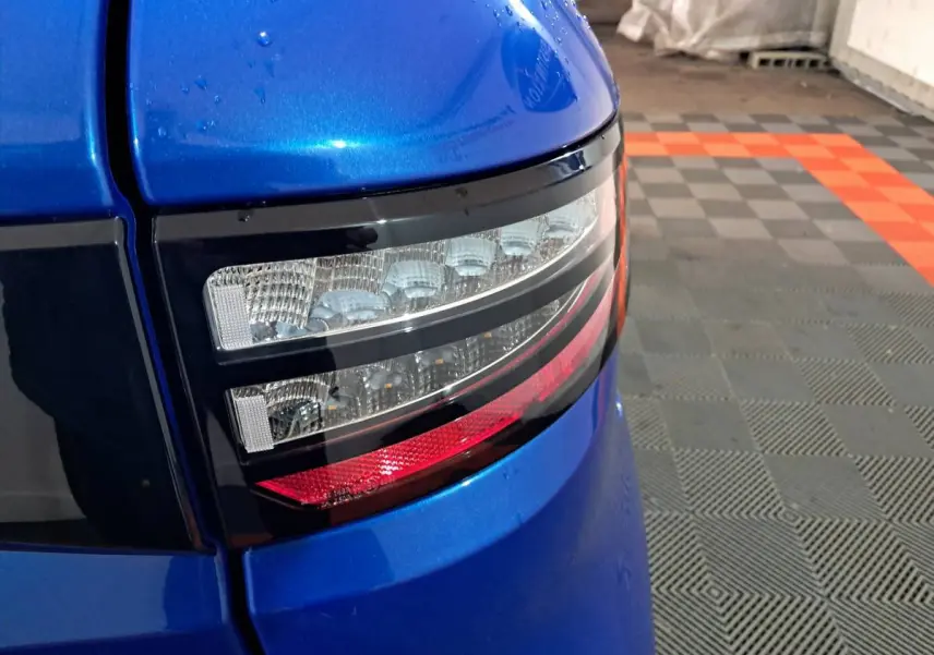 Gros plan sur le feu arrière droit bleu métallisé de l'AIXAM AMBITION 0.5 CITY GTO 2025 dans un garage.