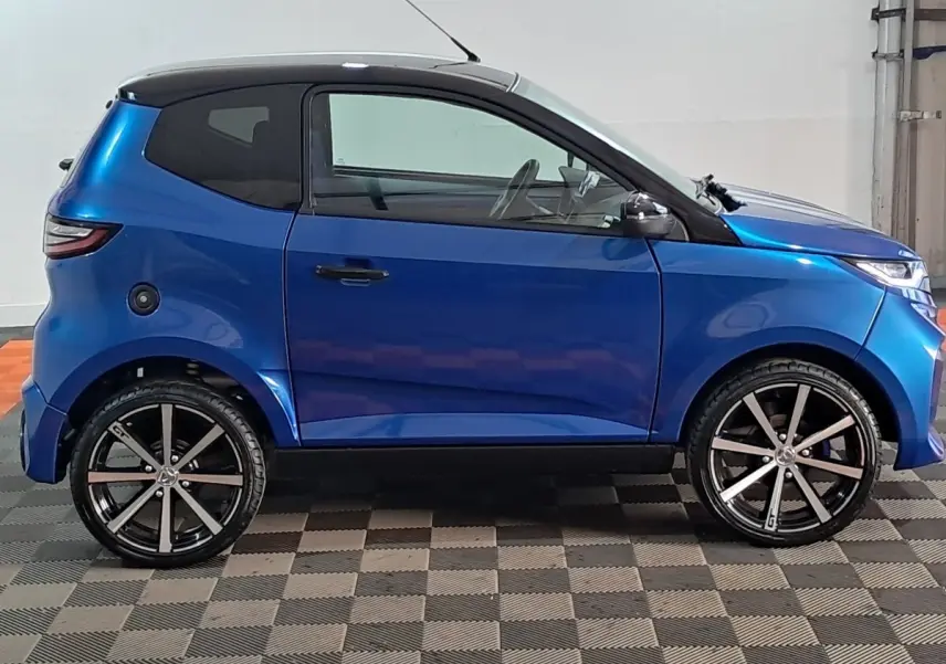 Profil côté gauche d'une Aixam Ambition 0.5 City GTO bleu 2025 avec jantes noires et rétroviseur caméra au conducteur.