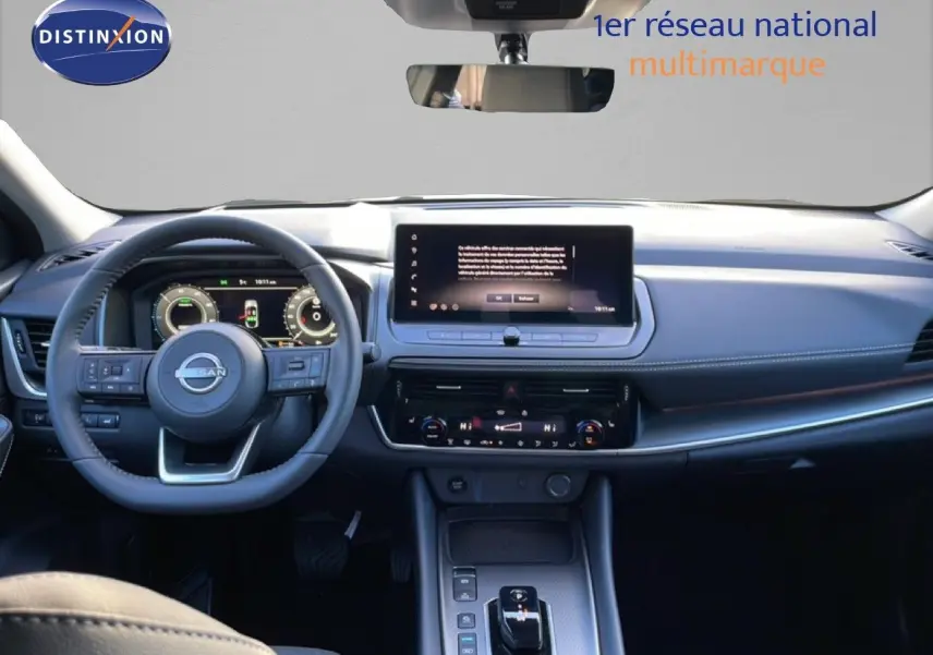 Vue intérieure avant du Nissan Qashqai 2025 gris argile métal, tableau de bord moderne avec écran tactile central et volant multifonction.