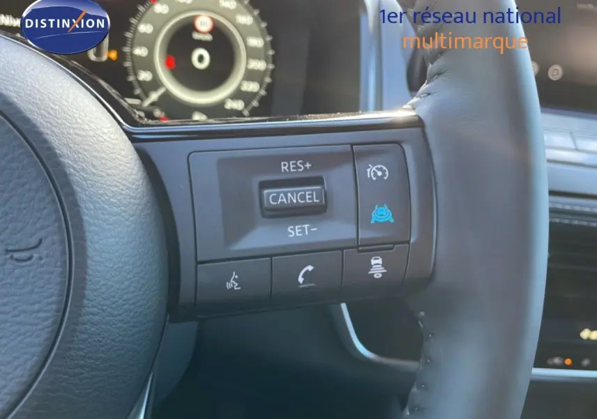 Gros plan sur le volant cuir noir du Nissan Qashqai gris argile, avec commandes de régulateur de vitesse et tableau de bord numérique visible.