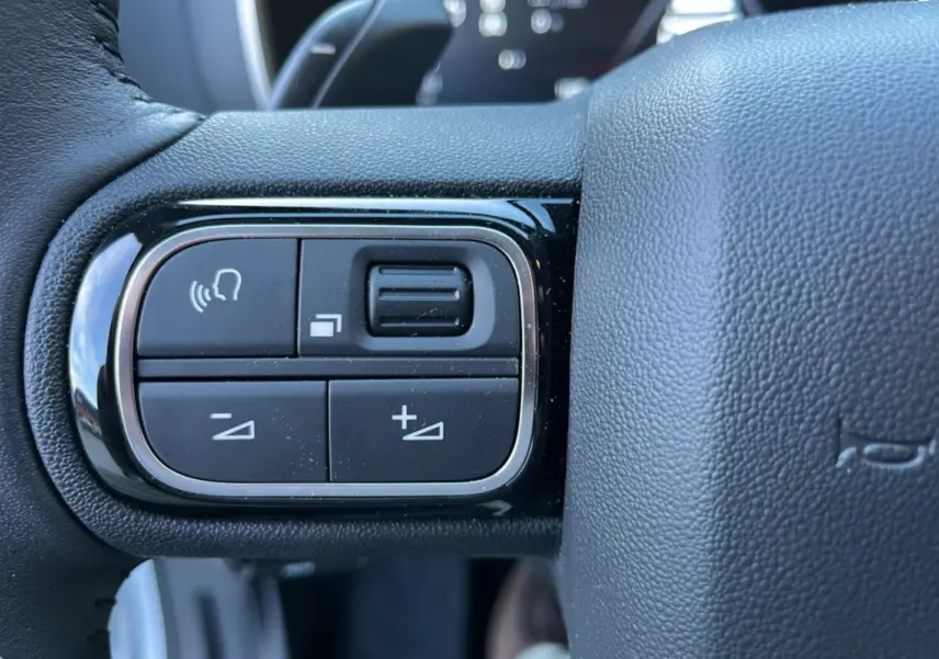 Gros plan sur les commandes vocales et de volume au volant cuir du Citroën C5 Aircross Hybrid blanc okénite.