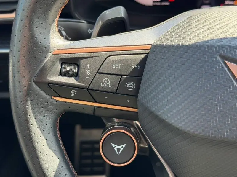 Gros plan sur le côté gauche du volant cuir perforé du CUPRA Formentor blanc, avec commandes multifonctions et logo CUPRA.