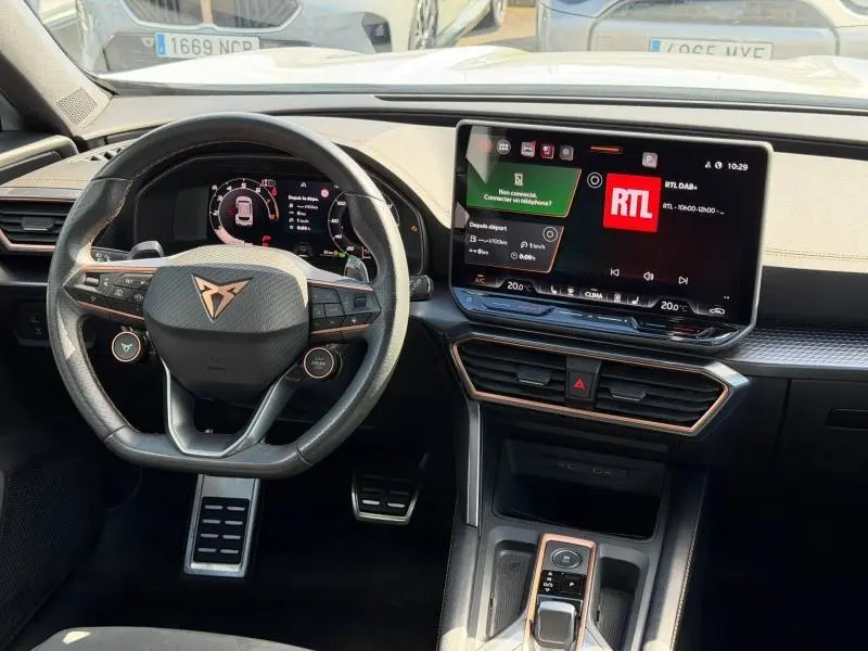 Vue intérieure frontale du tableau de bord et volant cuir noir avec logo CUPRA, écran tactile multifonction et pédalier sport.