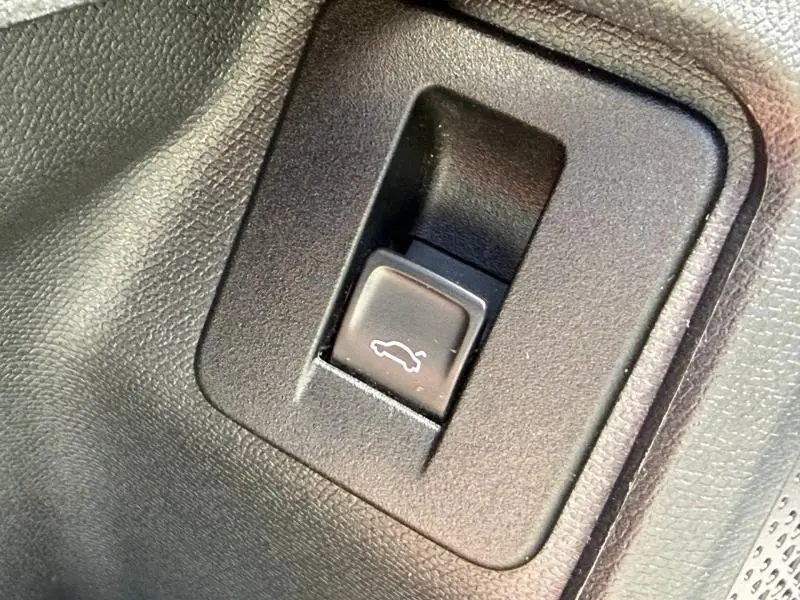 Gros plan sur le bouton d'ouverture électrique du coffre dans l'habitacle noir du CUPRA Formentor blanc Nevada.