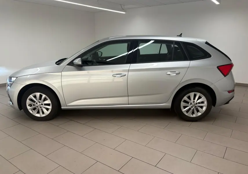 Vue de profil côté gauche d'une Skoda Scala gris argent 2024, version 1.0 TSI 110 DSG7 Business en intérieur showroom.
