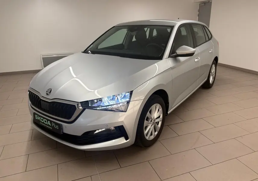 Vue 3/4 avant droite d'une Skoda Scala gris argent 2024 avec phares allumés dans un intérieur neutre.