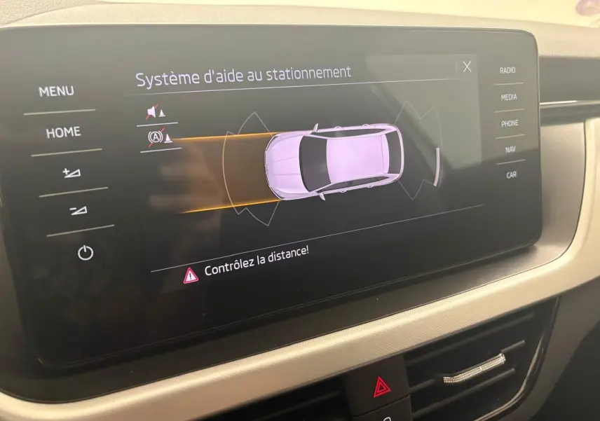 Écran central du Skoda Scala 2024 montrant le système d'aide au stationnement avec vue de dessus du véhicule gris argent.