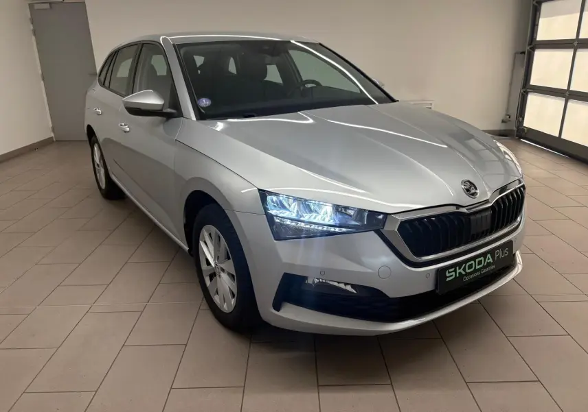 Vue 3/4 avant droite d'une Skoda Scala gris argent 2024 avec phares allumés dans un showroom intérieur.