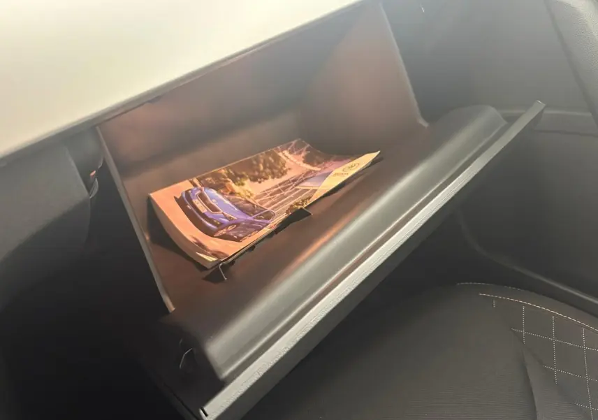 Vue intérieure du coffre à gants ouvert d'une Skoda Scala 2024, montrant une brochure avec une voiture bleue.