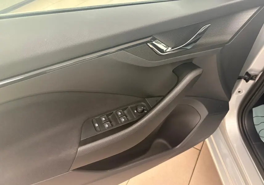 Vue intérieure côté conducteur de la porte d'une Skoda Scala gris argent 2024 avec commandes électriques des vitres et poignée chromée.