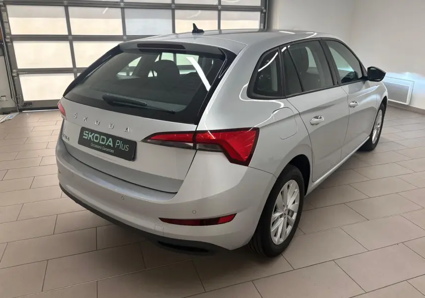 Vue 3/4 arrière droite d'une Skoda Scala gris argent 2024 en intérieur, avec feux arrière rouges et jantes argentées.