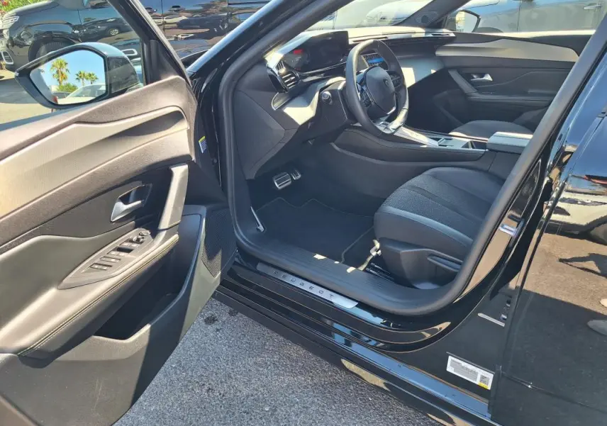 Intérieur côté conducteur d'une Peugeot 308 SW Hybrid noir, avec porte ouverte et cockpit numérique visible.