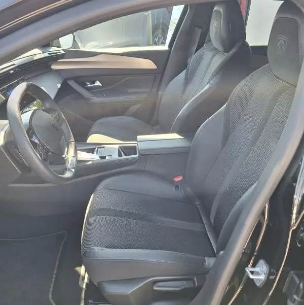 Vue intérieure côté conducteur du Peugeot 308 SW Hybrid 145 e-DCS6 GT 2025 noir, sièges sport avec logo embossé et cockpit numérique.