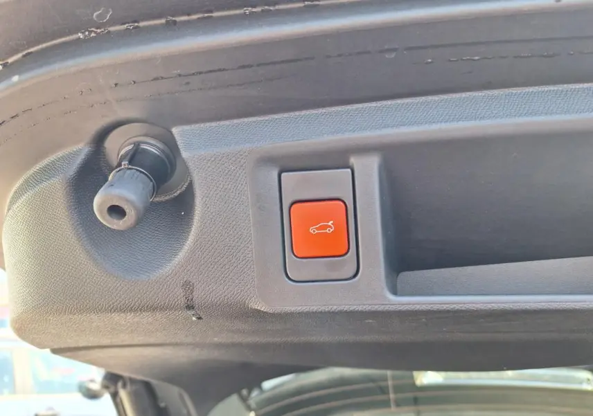 Gros plan sur le bouton rouge d'ouverture électrique du hayon du Peugeot 308 SW Hybrid noir, vue intérieure arrière.