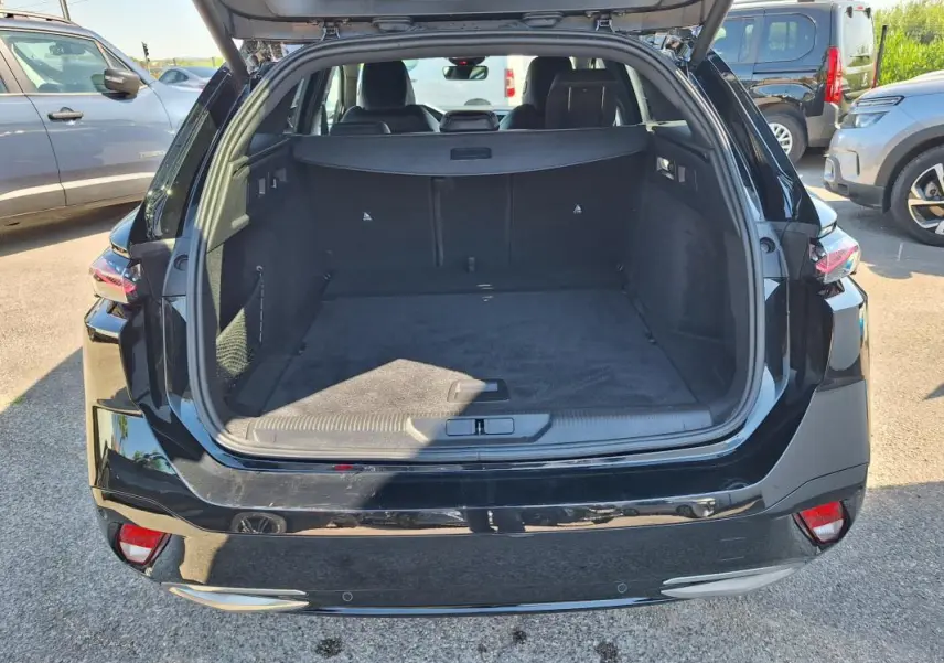 Coffre ouvert en vue arrière d’un Peugeot 308 SW Hybrid 145 noir, montrant un espace de chargement spacieux et propre.
