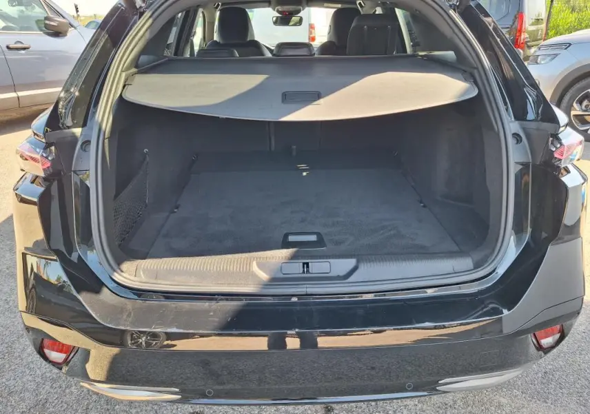 Coffre ouvert de la Peugeot 308 SW Hybrid 145 e-DCS6 GT noir, vue arrière montrant l’espace de chargement et la plage arrière.