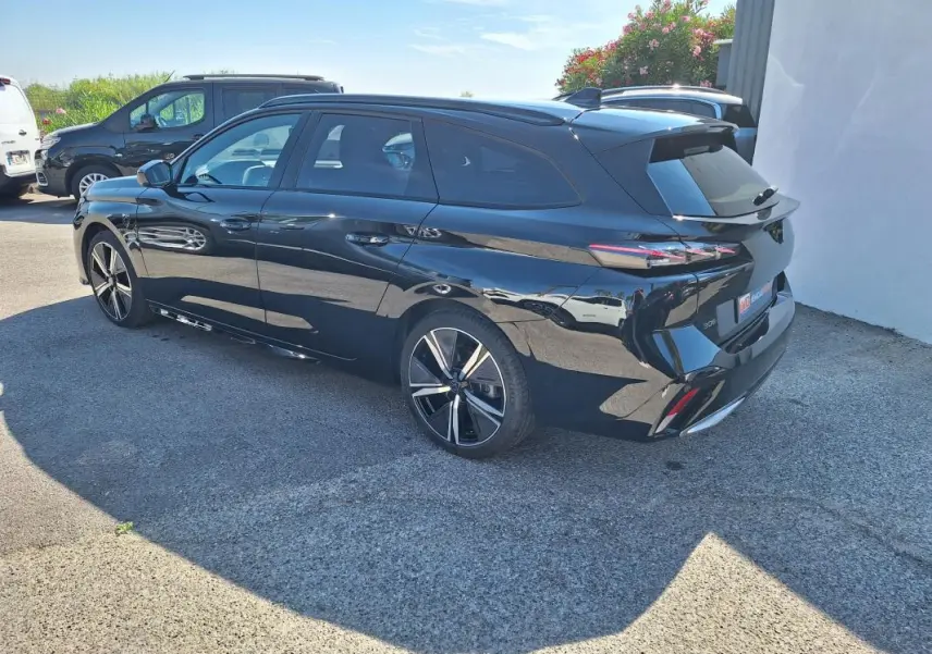 Peugeot 308 SW Hybrid noir vue 3/4 arrière droit, avec barres de toit et jantes alliage 18 pouces.