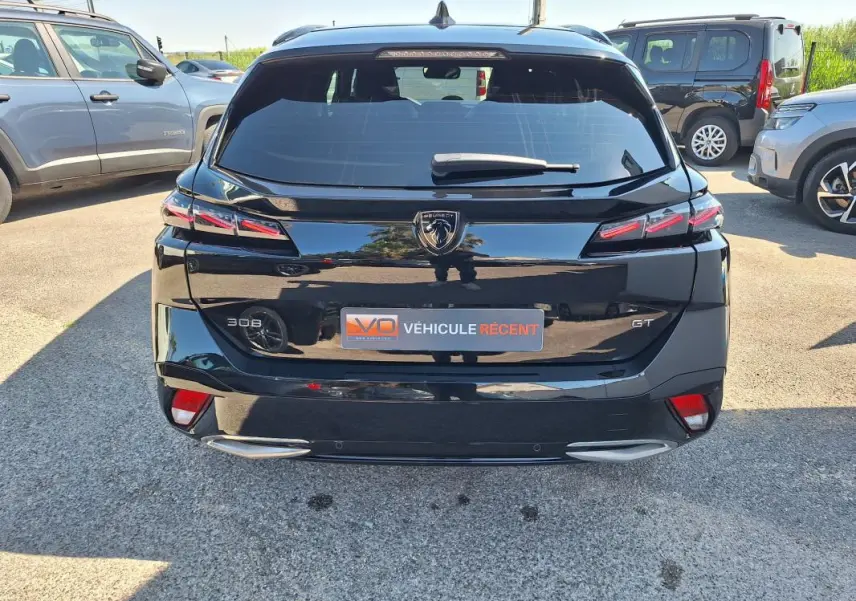 Vue arrière d’un Peugeot 308 SW Hybrid 145 e-DCS6 GT noir avec barres de toit et feux LED distinctifs.